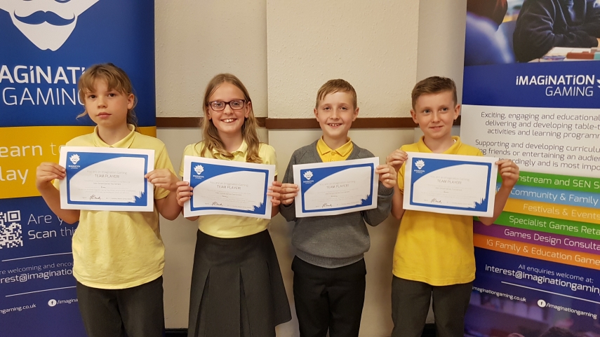 Four children wearing grey and yellow uniform holding Imagination Gaming certificates