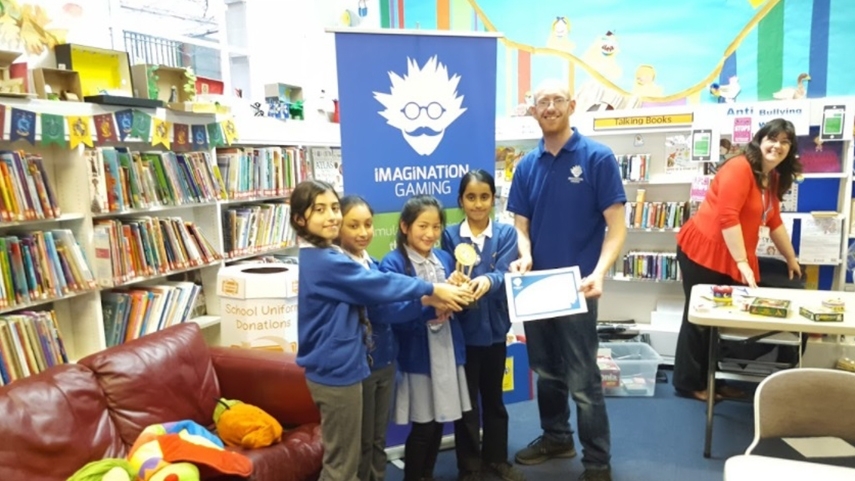 Group of school girls with certificate and trophy, stood next to a member of the Imagination Gaming staff